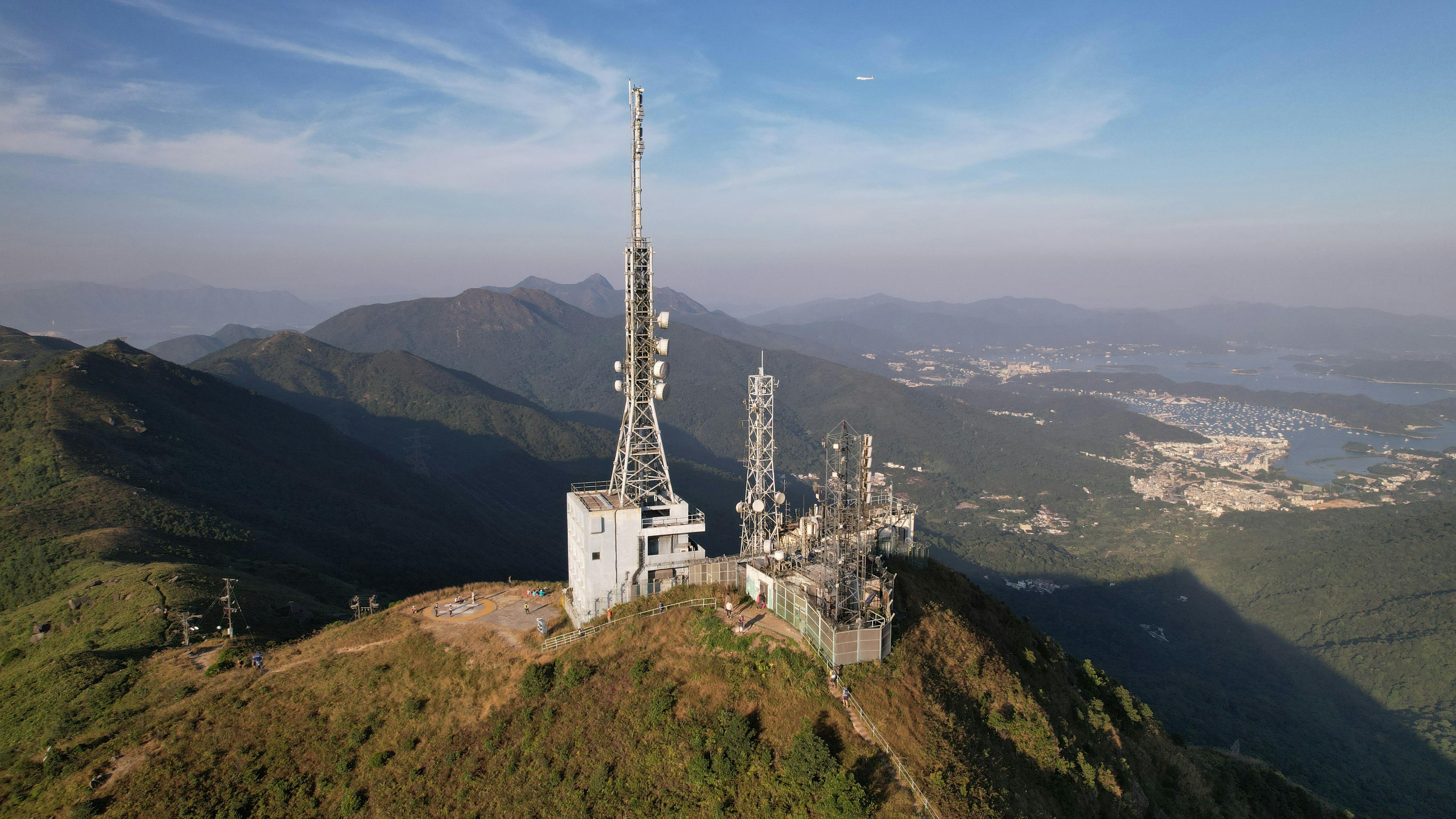 Telecommunication towers on a mountain peak with a scenic view of mountains and valleys.